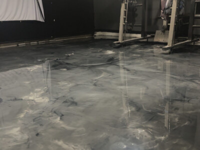 A gym room with weightlifting equipment and a polished, marbled gray epoxy floor.